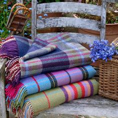 a pile of blankets sitting on top of a wooden bench next to a basket filled with flowers