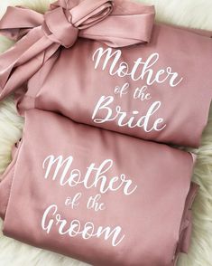 mother of the bride and groom embroidered on pink satin robes with matching bows, laying on a white furnishing