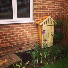 a small wooden outhouse sitting next to a brick wall with flowers growing in it