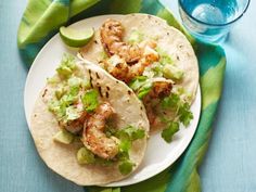 two shrimp tacos on a white plate next to a glass of water