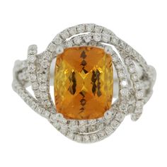 A brilliant ring featuring a GIA certified natural yellowish-orange sapphire! It weighs 4.84 carats and is free of any eye-visible inclusions allowing the stones natural brilliance and bright color to shine! It is shaped as a cushion and is accented by 1.18 carats of round brilliant-cut diamonds set in 18k white gold swirls around the ring and sapphire. Made in 18k white gold and ready to be worn! Ring Size 6 Yellow Diamond Fine Jewelry Gemstones, Orange Sapphire Ring For Formal Occasions, Orange Diamond Ring With Prong Setting, Fine Jewelry Orange Sapphire Anniversary Ring, Orange Sapphire Ring For Anniversary, Formal Orange Topaz Ring With Diamond, Fine Jewelry Orange Diamond Ring, Orange Citrine Topaz Ring, Orange Diamond Topaz Ring With Center Stone