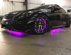 a black car with purple lights on it's rims in a garage area