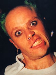 a man with green hair and piercings looks at the camera while wearing ear rings