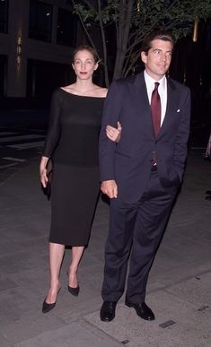 a man in a suit and tie walking next to a woman wearing a black dress