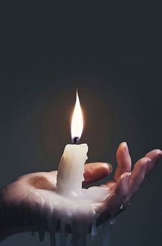 a hand holding a lit candle in it's palm with water dripping from the top