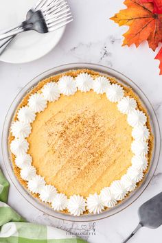 a pie sitting on top of a white table next to a fork and orange leaves