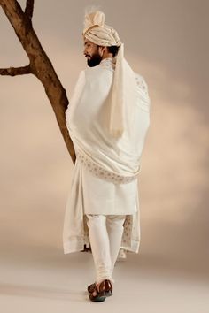 White full sleeves sherwani in linen silk base with all over Kashmiri Jamawar embroidery highlighted wih dabka and zari. Paired with full sleeves plain kurta, churidar, safa and embroidered border stole.
Components: 5
Pattern: Embroidery
Type Of Work: Zari, Dabka
Neckline: Band
Sleeve Type: Long
Fabric: Linen Silk
Color: White
Other Details: 
Closure: 
Sherwani: Front hooks
Kurta: Front placket buttons
Note: The jewellery and kalangi worn by the model is not for sale
Occasion: Groom - Aza Fashio White Sherwani, Embroidered Sherwani, Blouse Yoke, Personal Shopping Service, Dhoti Pants, Haldi Ceremony, Indian Wedding Outfits, Pashmina Shawl, Silk Embroidery