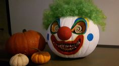 a clown's head next to a pumpkin with green hair on it and two smaller pumpkins