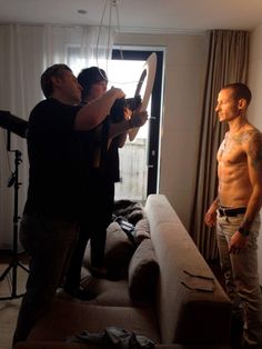 two men standing in a living room with one man holding an object up to the ceiling