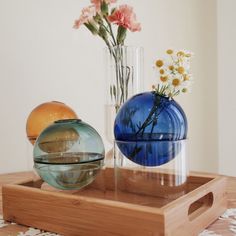 two vases with flowers in them sit on a wooden tray next to each other