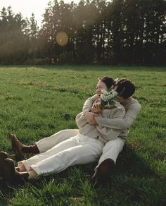 two people sitting in the grass hugging each other