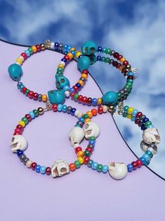 three bracelets with different colored beads and charms on top of a purple surface under a cloudy blue sky