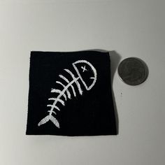 a coin sitting next to a small black piece of cloth with white stitching on it