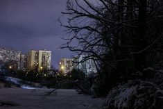 the city is lit up at night with snow on the ground and buildings in the background