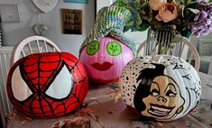 three painted pumpkins sitting on top of a table next to flowers and other decorations