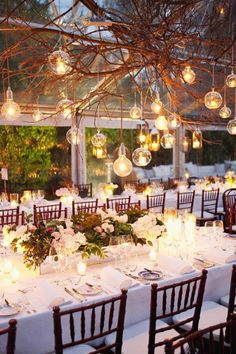 a dining room set up with white table cloths and flowers, hanging chandeliers over the tables