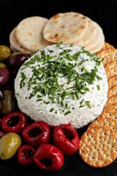 an assortment of crackers, olives, and cheese on a black platter