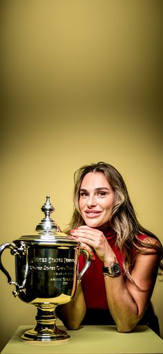 a woman in red shirt holding up a trophy on top of a green table next to a yellow wall