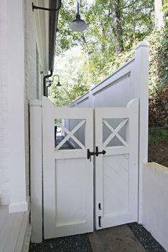 an open white gate on the side of a house with a light hanging above it