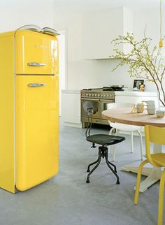 a yellow refrigerator sitting in the middle of a kitchen next to a table and chairs