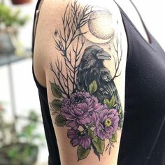 a woman with a tattoo on her arm has flowers and a crow in the background