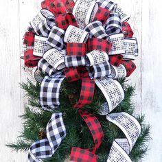 a red and black christmas wreath on top of a white wooden wall with pine cones