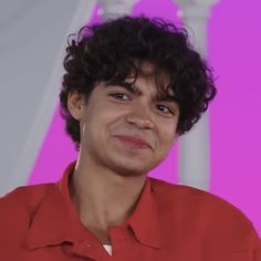 a close up of a person wearing a red shirt and looking at the camera with a smile on his face