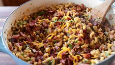 a pan filled with pasta and meats on top of a wooden table next to a spoon