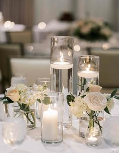 a table with candles and vases filled with white flowers on top of each other