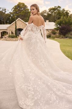 a woman in a white wedding dress standing on a driveway with her back to the camera