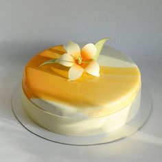 a yellow and white cake with a flower on it's top sitting on a plate