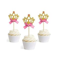 three cupcakes with gold crown toppers and pink bows are sitting next to each other