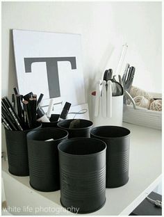 there are many black cups on the table with pens and pencils in them,