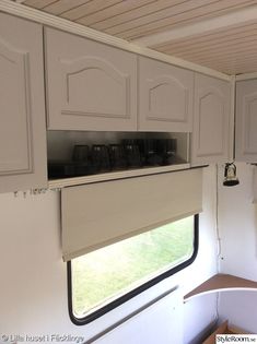 the inside of a camper with white cupboards and window blinds on it's side