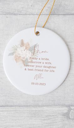 a ceramic ornament with the words mom and flowers on it, hanging from a gold chain