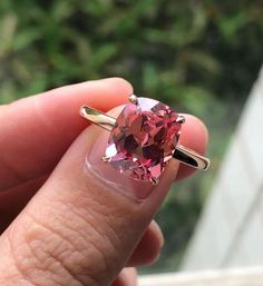 a woman's hand holding a ring with a pink heart shaped stone on it