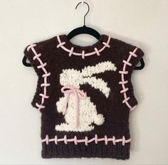 a knitted sweater hanging from a hook on a white wall with pink trimmings