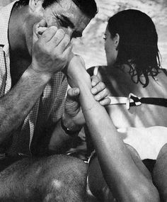 a man and woman sitting next to each other on the beach with their hands covering their mouths