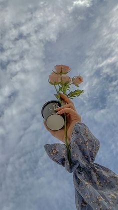 a person holding a flower in front of the sky with clouds behind them and a compact mirror on their left hand