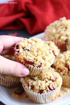 a person is picking up some cranberry muffins on a white plate