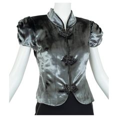 One part short sleeved evening jacket and one part formal top, the best part of this striking piece is neither its gleaming gunmetal finish nor its tulle-stuffed Renaissance sleeves; rather it is the black jeweled buttons, each of which is pinned to the fabric and therefore removable and wearable as a dress clip. Like getting eight pieces of jewelry as well as one formidable top. Princess cut evening jacket / top with ruched, tulle-lined short sleeves, Mandarin collar and cutaway front panels; b Formal Top, Formal Tops, Evening Jacket, Black Jewel, Balloon Sleeve Blouse, Dress Clip, Evening Jackets, Mandarin Collar, Princess Cut