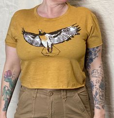 Our hand-drawn Red-Tailed Hawk design is printed in brown, white and orange on this super soft, raw-edge gold tee.   Available in  XS -2XL.  Runs a little small, order up for a slouchier fit. Model is a medium/ large and wearing a large.  See size chart and message me with any questions.  Soft, lightweight 65%Poly/35%Cotton, sweatshop free. Our original, hand-drawn designs are printed on sweat-shop free clothing using environmentally conscious water-based inks. Each item is individually hand-scr Hand Printed Relaxed Fit Short Sleeve Tops, Vintage Hand Printed Crew Neck Tops, Relaxed Fit Hand Printed Short Sleeve Tops, Hand Printed Short Sleeve Tops With Relaxed Fit, Hand Printed Crew Neck Graphic Tee, Brown Short Sleeve Tops With Screen Print, Hand Printed Graphic Tee With Crew Neck, Brown Short Sleeve Top With Screen Print, Hand Printed Short Sleeve Graphic Tee