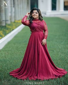 a woman in a long red dress posing for a photo on the grass with her hands behind her head