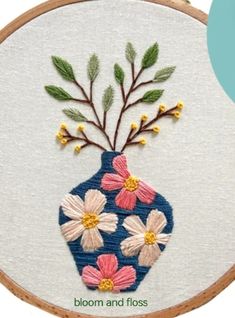 a blue vase with pink and white flowers in it on a wooden hoop next to a wall hanging