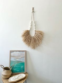 a table with a vase on it next to a painting and a necklace hanging from the wall