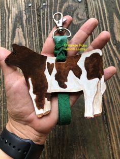 a hand holding a brown and white cow keychain with a green ribbon on it