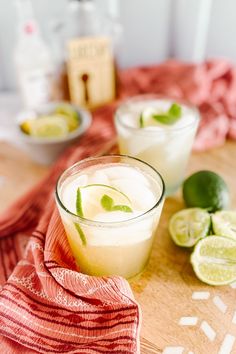 two glasses filled with lemonade sitting on top of a wooden table next to sliced limes