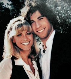 a young man and woman are posing for a photo in front of some trees with their arms around each other