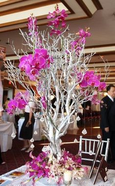 the table is decorated with purple flowers and white branches, while people are standing in the background