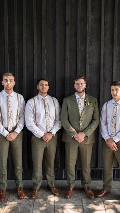 four men wearing ties and vests standing in front of a wooden fence with their arms crossed